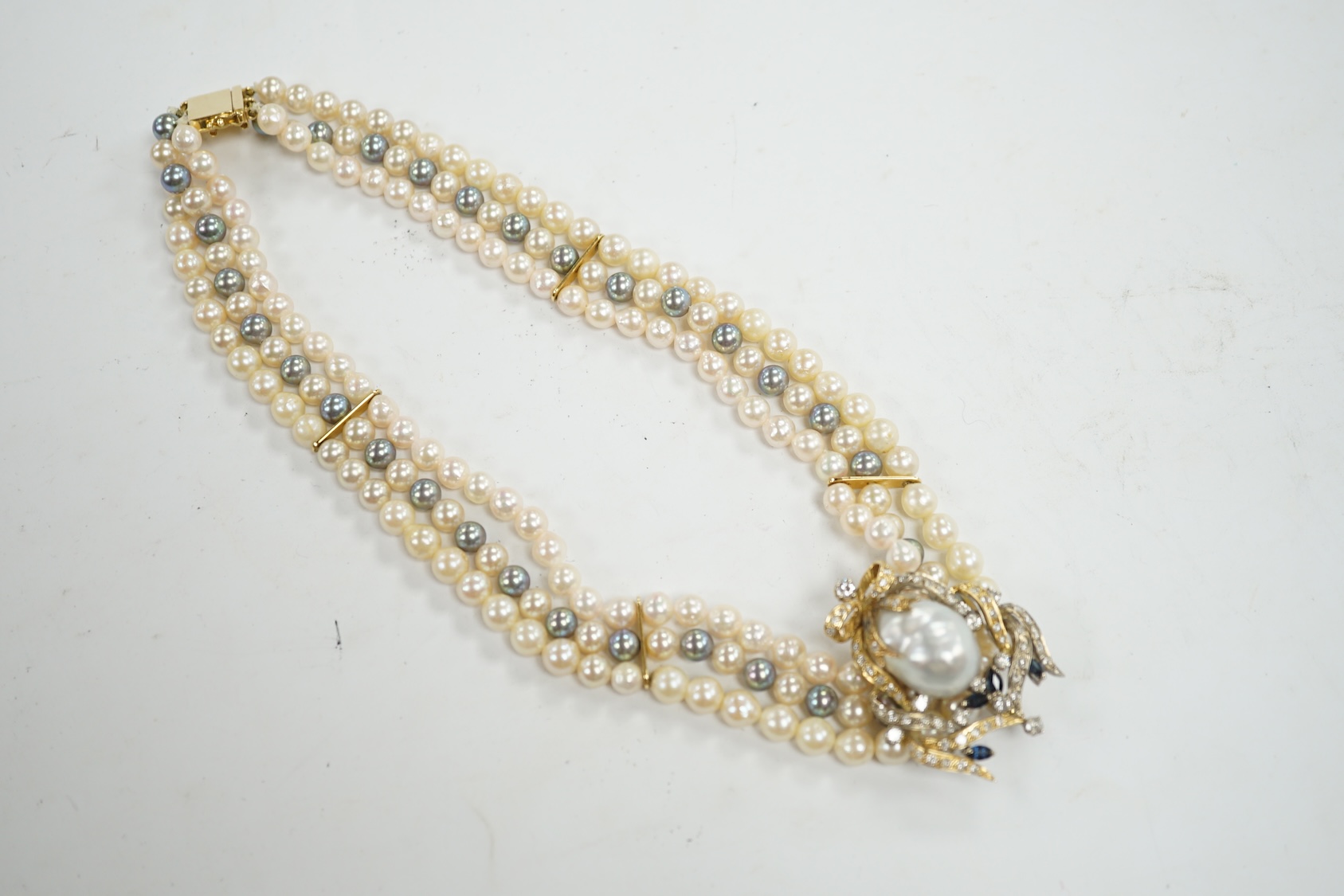 A modern triple strand two colour cultured pearl necklace, with yellow metal clasp and detachable yellow metal baroque pearl, sapphire and diamond cluster set clip, 43cm, gross weight 101.9 grams. Condition - fair to goo